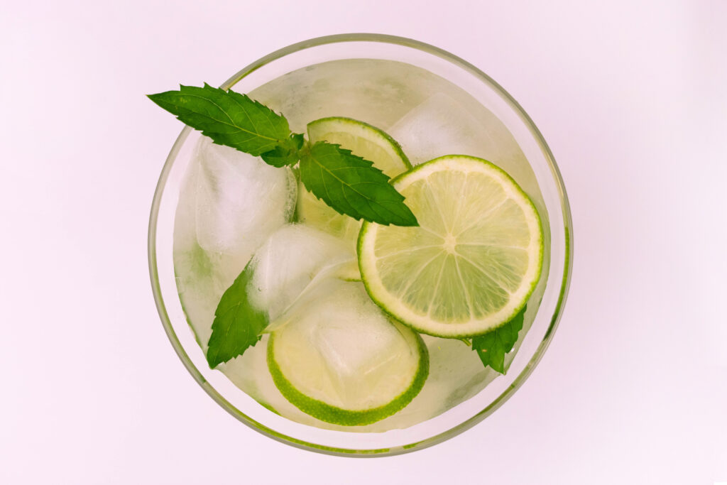 Green iced tea with fresh lime slices and mint leaves, displayed on a white background.